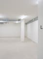 Empty underground garage space, white walls, ceiling pipes, two entrance doors.