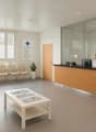 Clean and bright reception area with a desk, chairs, books on a table, a plant, and a TV monitor displaying a logo on the wall.