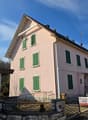 2-story pink house with green shutters, garage, and a stone wall in the front