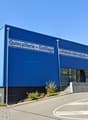 Large blue and white building with the sign 'Carrel Quincaillerie Outillage' indicating it is a hardware and tools store. There is a parking area in front of the building.