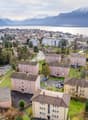 Aerial view of apartment buildings, some with parking areas, set in a picturesque location with mountains and a lake in the background.