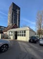 Commercial area with several cars parked in front of the building, a tall skyscraper behind, garage with multiple windows