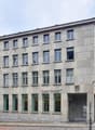 3 story building, concrete exterior, many windows, entrance at street level, flag at entrance