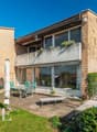 Modern house with brick facade, large windows, balcony, outdoor dining area, swimming pool, garden