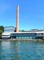 modern architectural building with glass windows and a tall chimney, set on a waterfront with a boat visible
