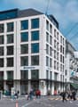 Modern white building with glass windows, multiple floors, and a blue sign reading 'Z ZURICH', located in a busy city street with people walking and streetlights.