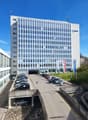 White building, glass windows, many floors, parking lot in front, street view