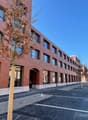 Red brick building, glass windows, modern design, multiple doors, empty parking lot, a tree in front