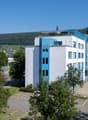 modern multi-story building, white exterior, blue accents, parking lot, scenic mountain view, several windows, entrance with steps