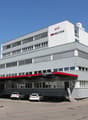 A multi-story commercial building with the Technomag logo prominently displayed. The building has large windows and a parking area in front.