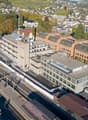 multi-story building with a slanted roof, close to the train station, several other buildings in the background
