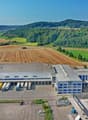 Large industrial building with multiple loading docks, surrounded by parking lots, trucks, and a vast green landscape.