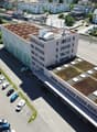 Large office building with green roof, cars parked in front of the building, adjacent parking lot.