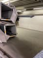 The image shows a storage room or utility area with several large storage containers or bins stacked on shelves. The room has a concrete floor and exposed ceiling beams, indicating an industrial or utilitarian space.