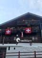 2-story wooden chalet-style building with balconies, Swiss flags displayed, and a sign for the 'Restaurant Obermatt'