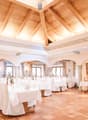 Large dining room with high wooden ceiling, ornate molding, arched windows, white tablecloths, and a fireplace