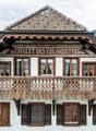 Facade of a chalet with an upper terrace supported by wooden structures and various windows
