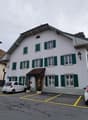 white house, green shutters, brown roof, parking lot, 2 cars parked