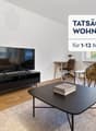 Spacious living room with hardwood floors, large windows, TV stand, coffee table, and a comfortable armchair. The room has a modern and minimalist design.