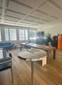 The image shows a spacious open-plan living area with a kitchen, dining, and living room. The space features hardwood floors, a coffered ceiling, large windows, and a mix of modern and rustic furnishings. The kitchen area includes a dishwasher and a priva