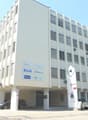 Large office building, white walls, multiple floors, glass windows, underground parking, multiple cars parked.