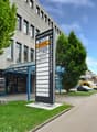 office building with glass walls, 2 story, large trees in front, car parked on street, sign board