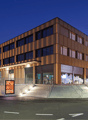 modern multi-story building, brown exterior, glass windows, ground-level storefront, stairs, parking sign