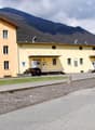 Yellow building, multiple windows, cars parked in front, mountains in the background
