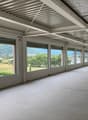 Empty room with large windows, tiled floor, metal ceiling, view of a field and mountains
