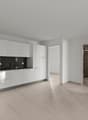 Modern, open-concept kitchen with white cabinets, black countertops, and stainless steel appliances. The kitchen leads into a larger living space with tiled flooring.