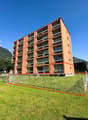 large orange building, many balconies, large red square outlined, tall green trees, grassy ground, mountains in background