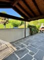 Terrace with wooden roof, fireplace, paved floor, wall, greenery, garden.