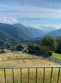 panoramic view, green field, mountains, road, houses, fenced area, car parked, clear blue sky