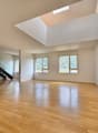 Spacious living room with hardwood floors, white walls, and a skylight providing natural light. The room has a clean, open layout.