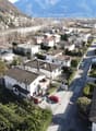 Aerial view of multiple houses with red cars parked outside, tiled roofs, driveways, and small gardens with trees