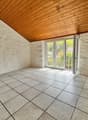 A room with white tiled floor and white walls, a glass door, wooden ceiling and an electric outlet on the wall.