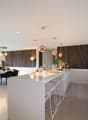 modern interior, white countertops, open-plan, large windows, large dining table, 2 stools, 2 couches, wooden wall, chandeliers
