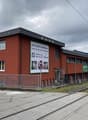 A multi-story red brick building with a flat roof, located next to a train track. The building appears to be a commercial or industrial facility.