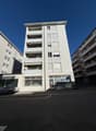modern white building with 4 floors, balcony, car parked in front, ground floor commercial space