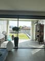 Spacious living room with large sliding glass doors leading to a balcony or terrace, hardwood floors, modern furniture including a sofa and armchair, decorative artwork on the walls, and a shelving unit with various decor items.