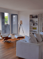 Living room, white walls, hardwood floor, glass door to terrace, white couch, armchair, books on shelf, lamp, plants