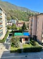 Detached house, concrete wall, green tarpaulin on the roof, entrance, fenced yard, street, green bushes, multi-story buildings in the background, distant mountains