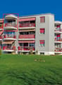 Multi-story building, grey exterior, red balconies, green front lawn, mountain backdrop