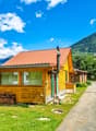 wooden house, metal roof, window shutters, green lawn, mountains in background