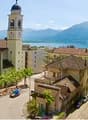 Church with a bell tower, several houses, road, lake, mountains in the background