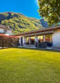 Two houses, with white walls, green lawn, mountain in the background
