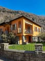 2-story house, orange exterior, brick wall foundation, multiple windows, fenced lawn, car parked, balcony on the first floor
