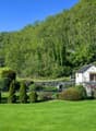 large house with garden, well-maintained green lawn, surrounded by trees, mountains in the background