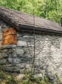 Stone house, brown roof, wooden door, surrounded by trees