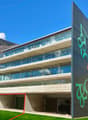 Modern building with glass windows, concrete structure, graffiti on the wall, green lawn, mountains in the background